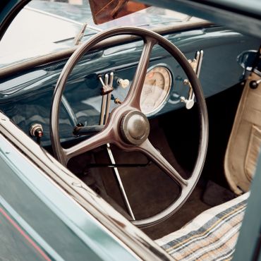 Steering wheel and dashboard of a vintage car with a plaid seat cover.