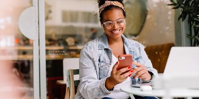 Smiling woman using phone in a cozy cafe with laptop nearby.