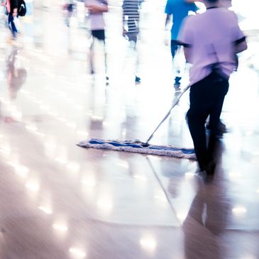 A person mopping a shiny floor in a busy indoor area.