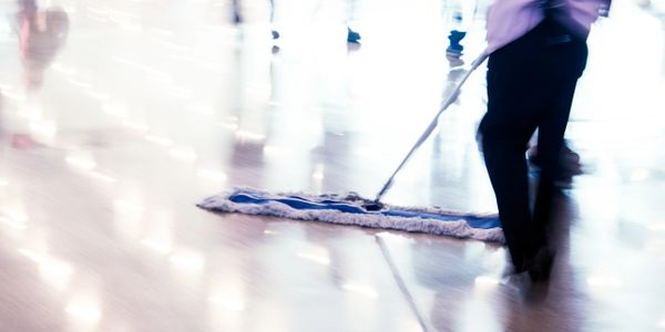 Person mopping a shiny floor in a busy indoor space.
