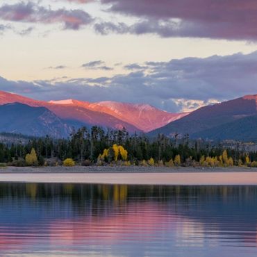 Sunset over a mountain lake with vibrant clouds reflecting on calm water.