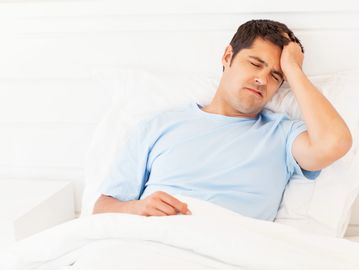Man looking unwell in bed holding his head.