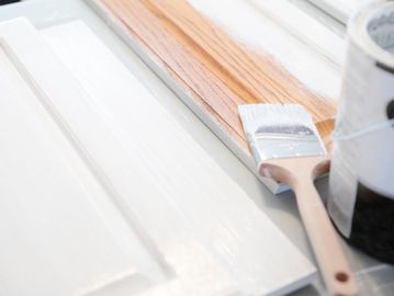 Painting a wooden door white with a paintbrush and can.