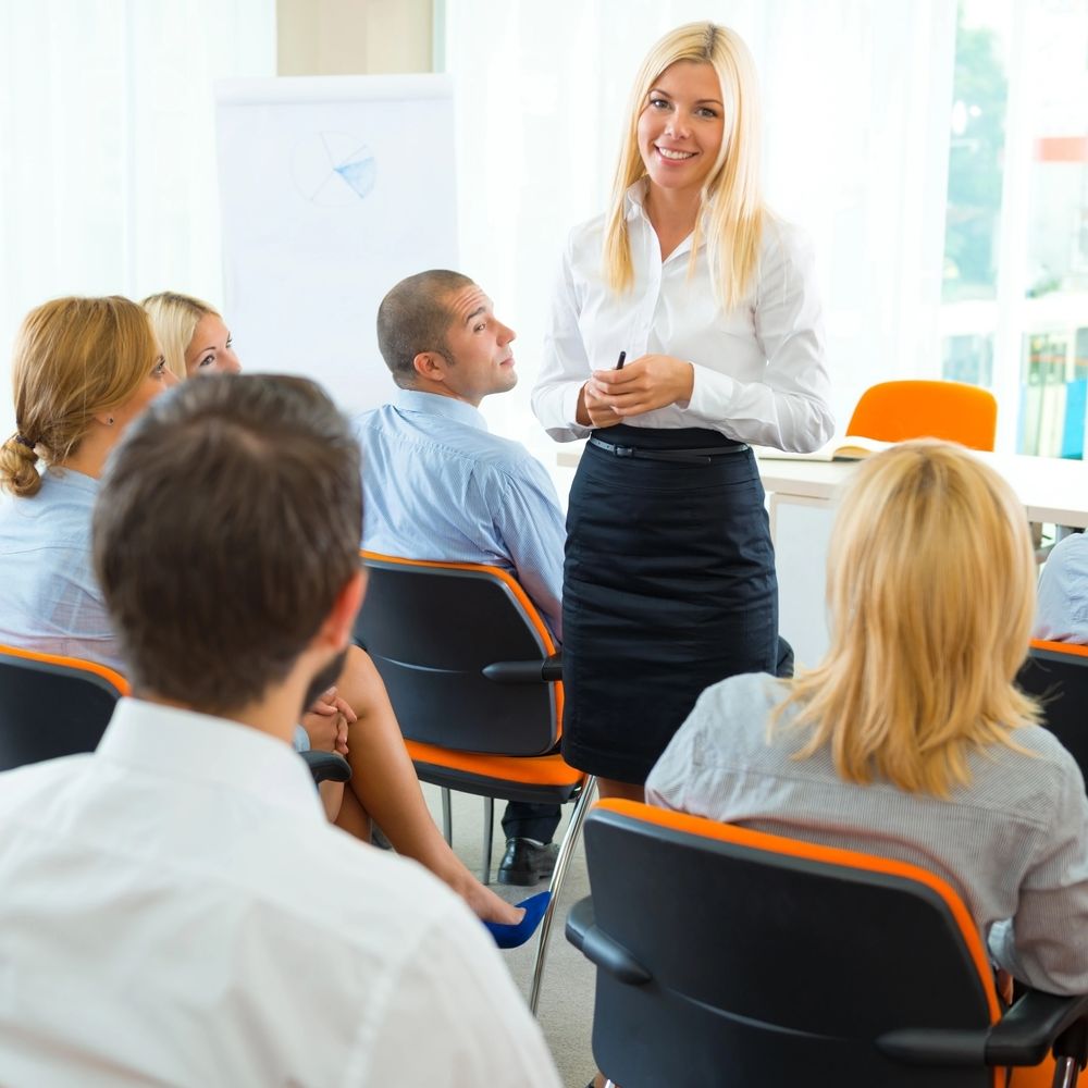 A woman in a white shirt presenting to a group in a bright office.