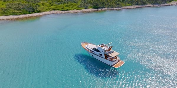 A luxury yacht sails on clear turquoise waters near a green shoreline.