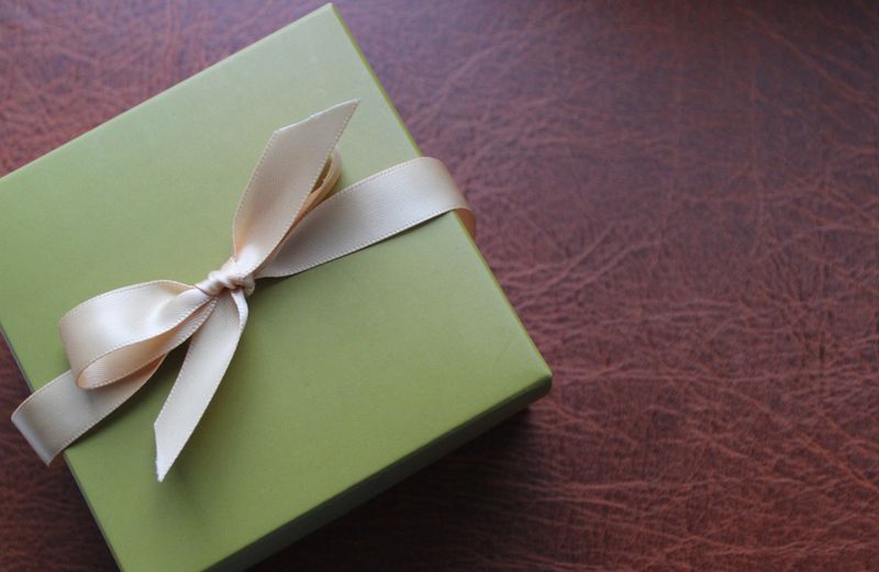 Business gift wrapping in olive tones with an elegant beige ribbon on brown leather