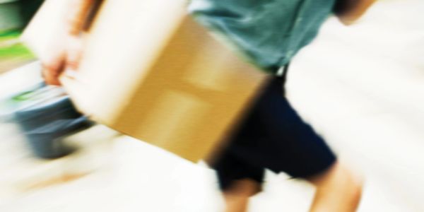 Blurred image of a person carrying a cardboard box while moving.