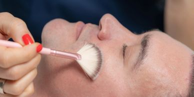 Applying makeup on a woman's face with a fan brush.