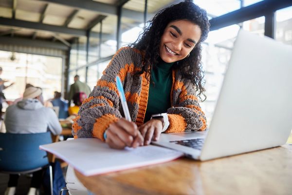 Smiling woman writing notes with laptop open.