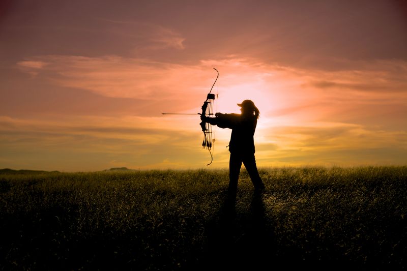 a bowhunter silhouetted against a brilliant sunset