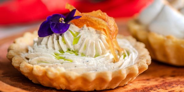 A tart topped with cream, edible flower, and garnish.