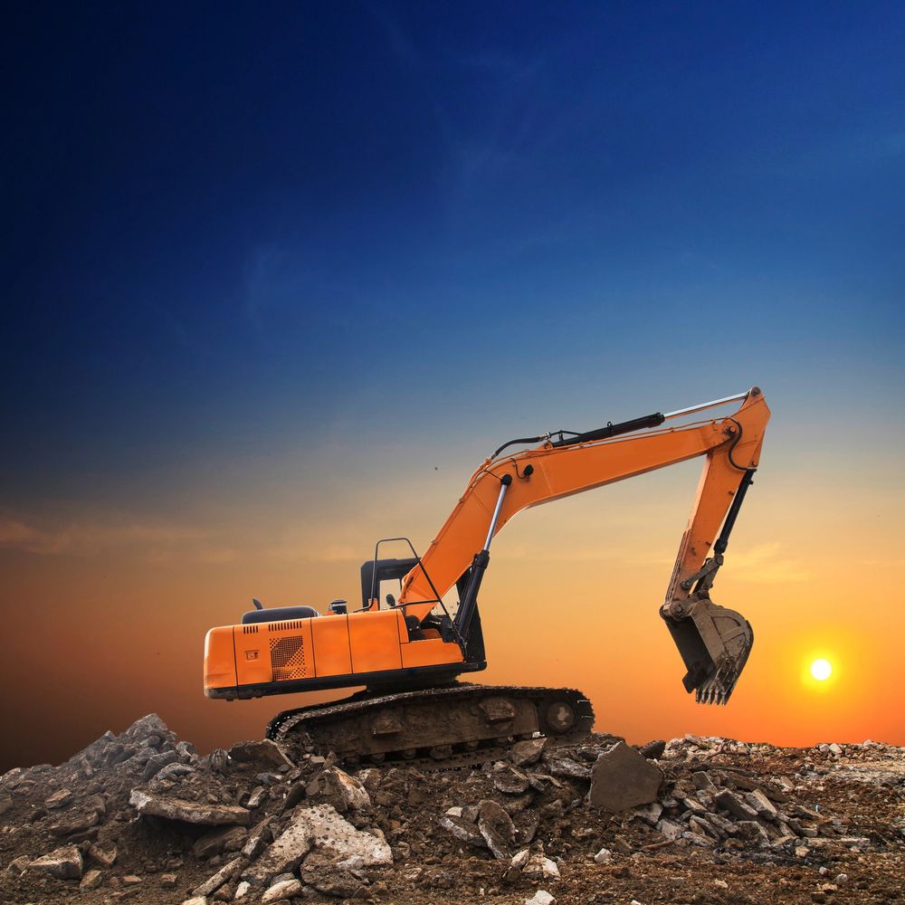Orange excavator on rocky terrain at sunset.