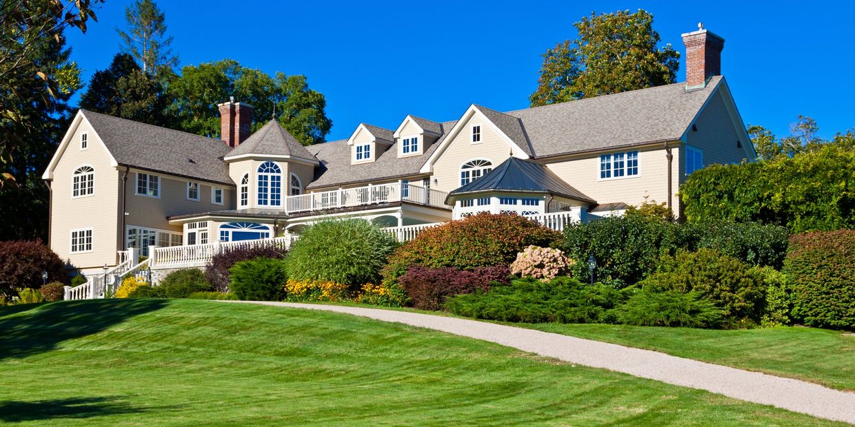 Large, elegant colonial-style home with beige siding, multiple chimneys, and a well-manicured lawn.