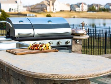 Outdoor kitchen with stainless steel grill and skewers on a wooden board.