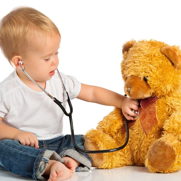 Toddler playing doctor using a stethoscope on a teddy bear.