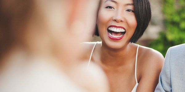 A woman with short hair laughing joyfully outdoors.