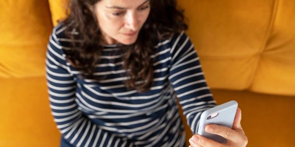 Woman with striped shirt looking at phone on yellow couch.