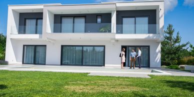 Three people standing outside a modern two-story house with large windows.