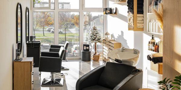 Modern hair salon with black chairs and large windows letting in natural light.