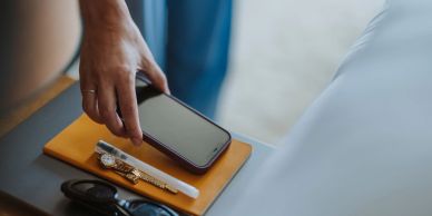 Person reaching for smartphone on bedside table.