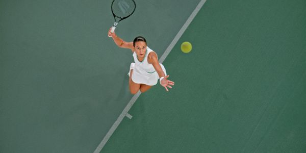 Tennis player reaching to hit the ball mid-air.