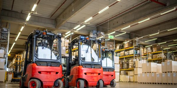 Three red forklifts parked in a well-organized warehouse with stacked shelves.