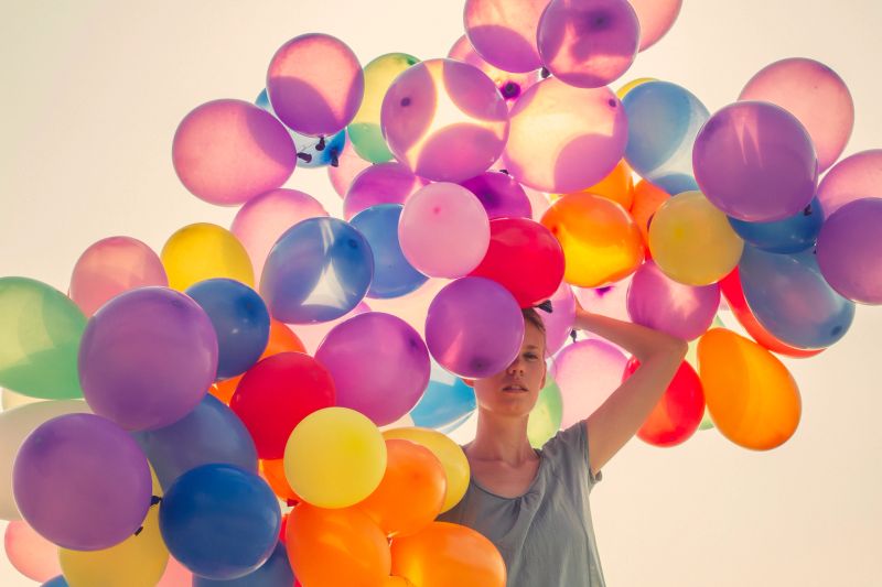 Young woman walking with big bunch o balloons in sunset