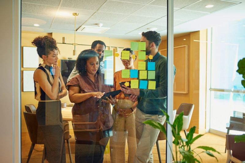 A group of diverse professionals brainstorm ideas in a modern office space. They are using sticky notes to organize their thoughts.