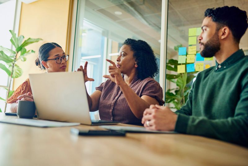 A diverse group of professionals brainstorming ideas in a modern office. They are looking at a laptop and discussing something.