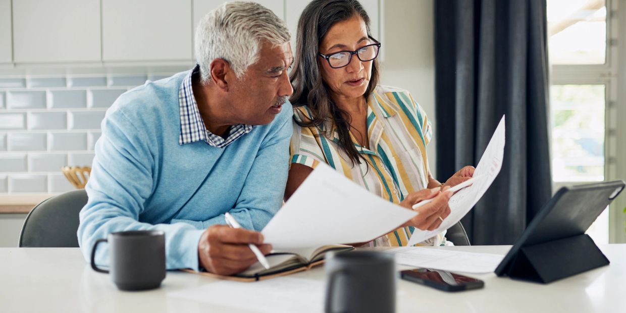 A mature couple reviewing documents together at a table with a tablet and coffee mugs.