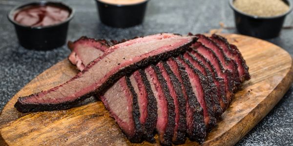 Sliced smoked brisket on a wooden cutting board with sauces in the background.