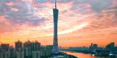 Sunset over a city skyline with a tall tower by the river.