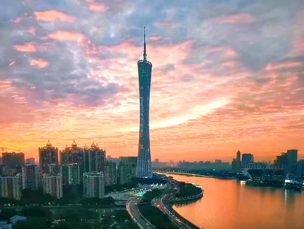 City skyline at sunset with a tall tower by a winding river.
