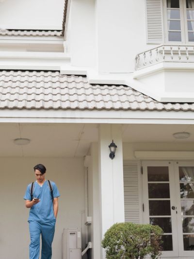 Person in blue scrubs walking outside a white house.