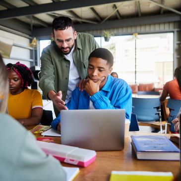Teacher helping student with laptop in classroom.