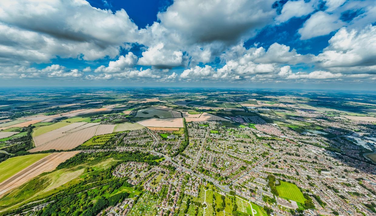Aerial view of suburban neighborhood and farmlands under a blue sky with clouds.