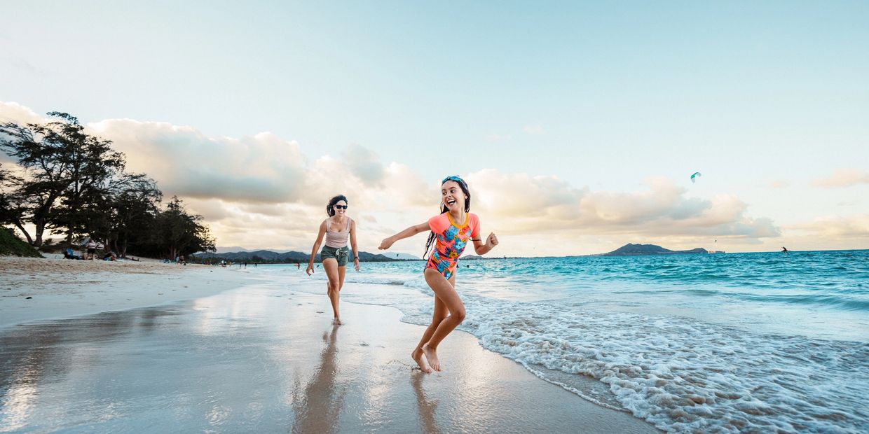 Child happily running on the beach with an adult following.