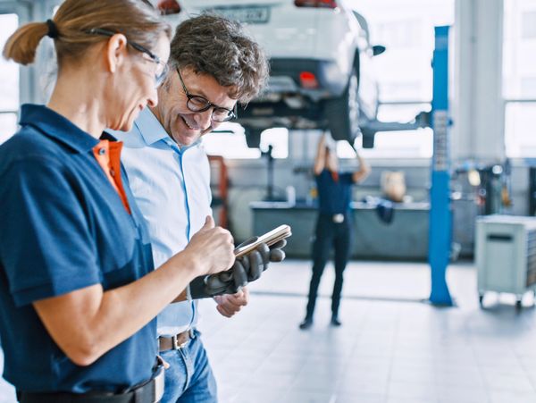 Two people discussing something on a tablet in a car repair shop.