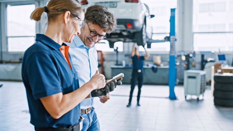 Manager And Mechanic Engage In Planning Discussion Using A Mobile Phone In The Auto Repair Shop