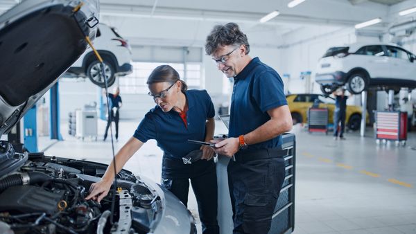 Two mechanics inspecting a car engine in a repair shop.
