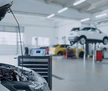 Mechanic diagnosing a car engine with a laptop and multimeter.
