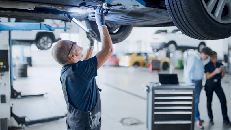 Male Mechanic Uses A Light Source While Working Underneath A Car In The Auto Repair Shop