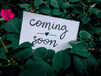 A handwritten note saying 'coming soon' placed among green leaves.