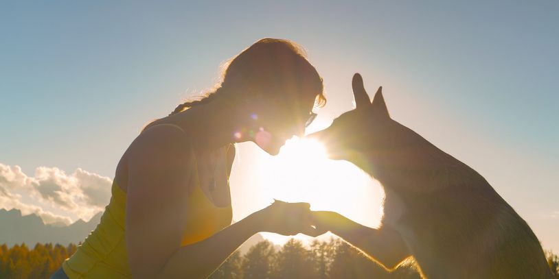 A woman and her dog share a tender moment at sunset outdoors.