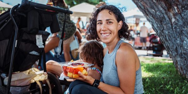 Smiling woman holding a container of fruit at an outdoor market.