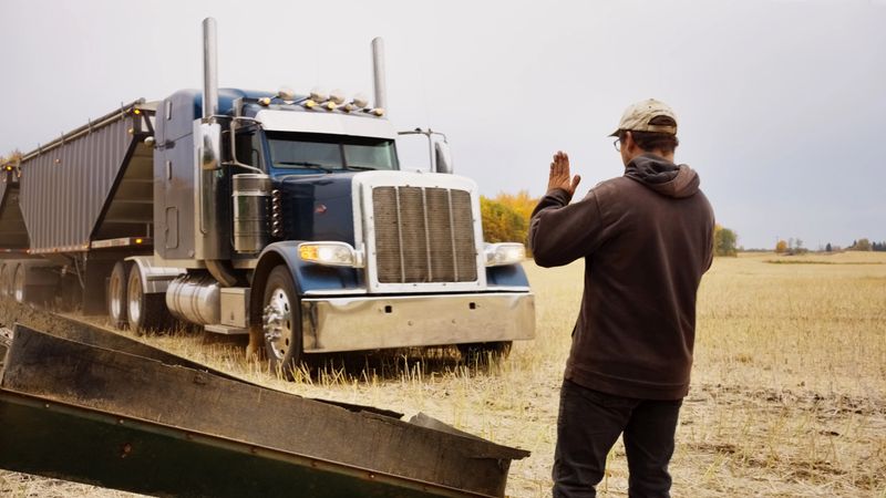 Rear view of man guiding a grain trailer truck to align along the grain storage silos while working on farm