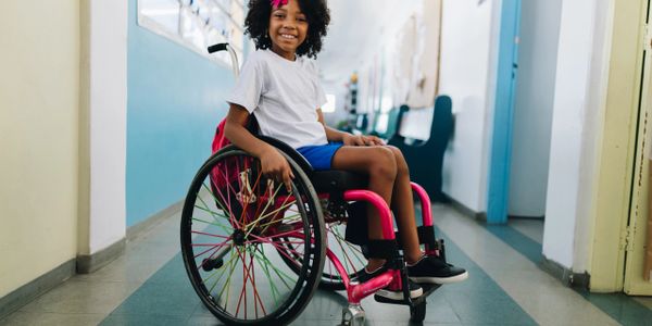 Smiling girl in a wheelchair in a bright hallway.