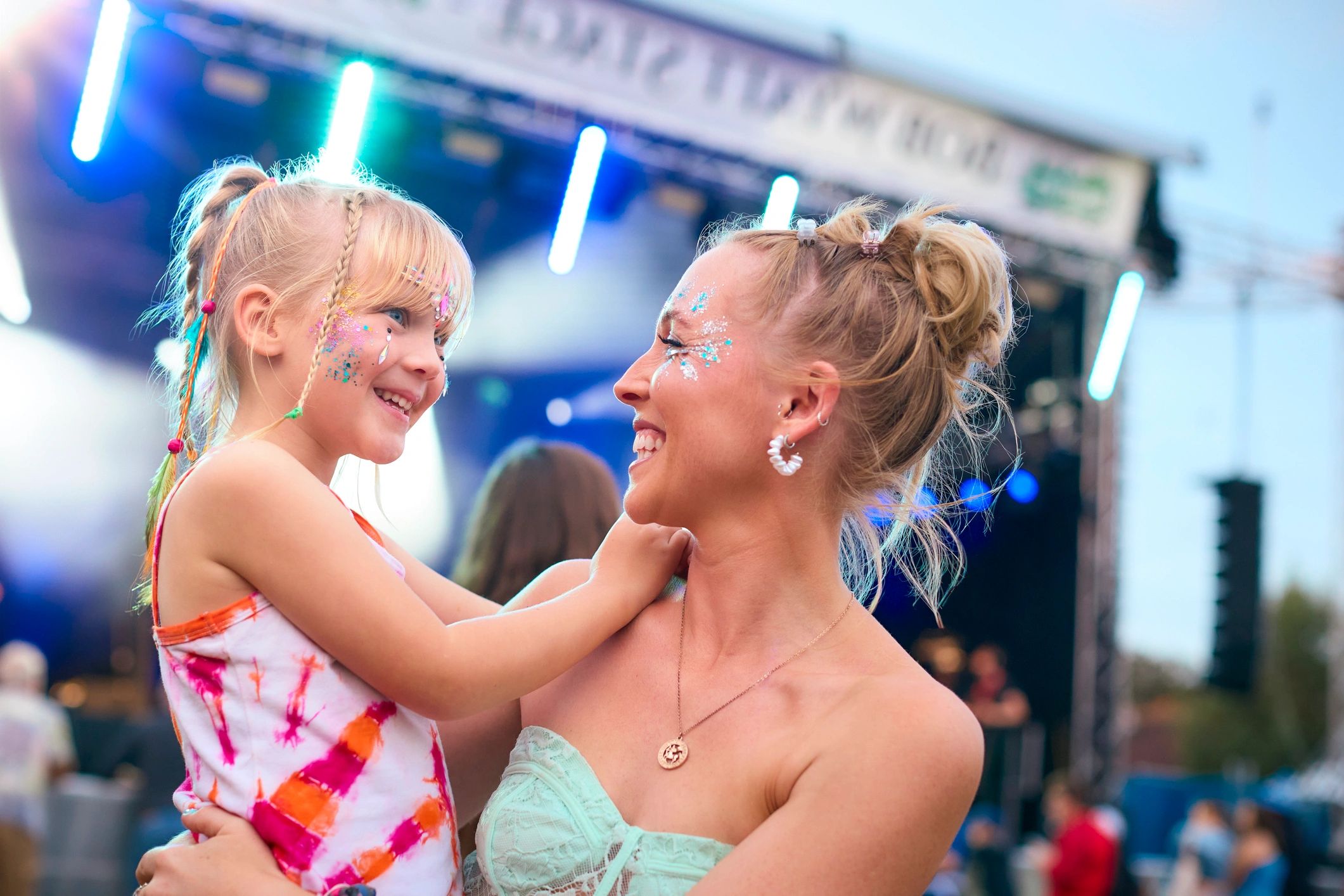 Mother and daughter with glitter face paint smiling at each other.