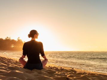 Woman meditating on the beach during sunrise.