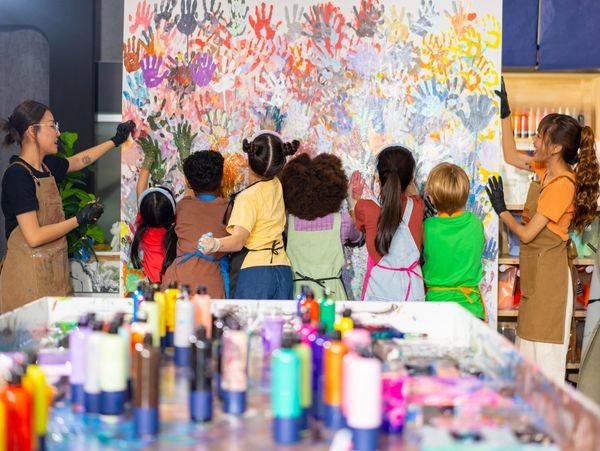 Children and teachers creating a colorful handprint mural together in an art studio.
